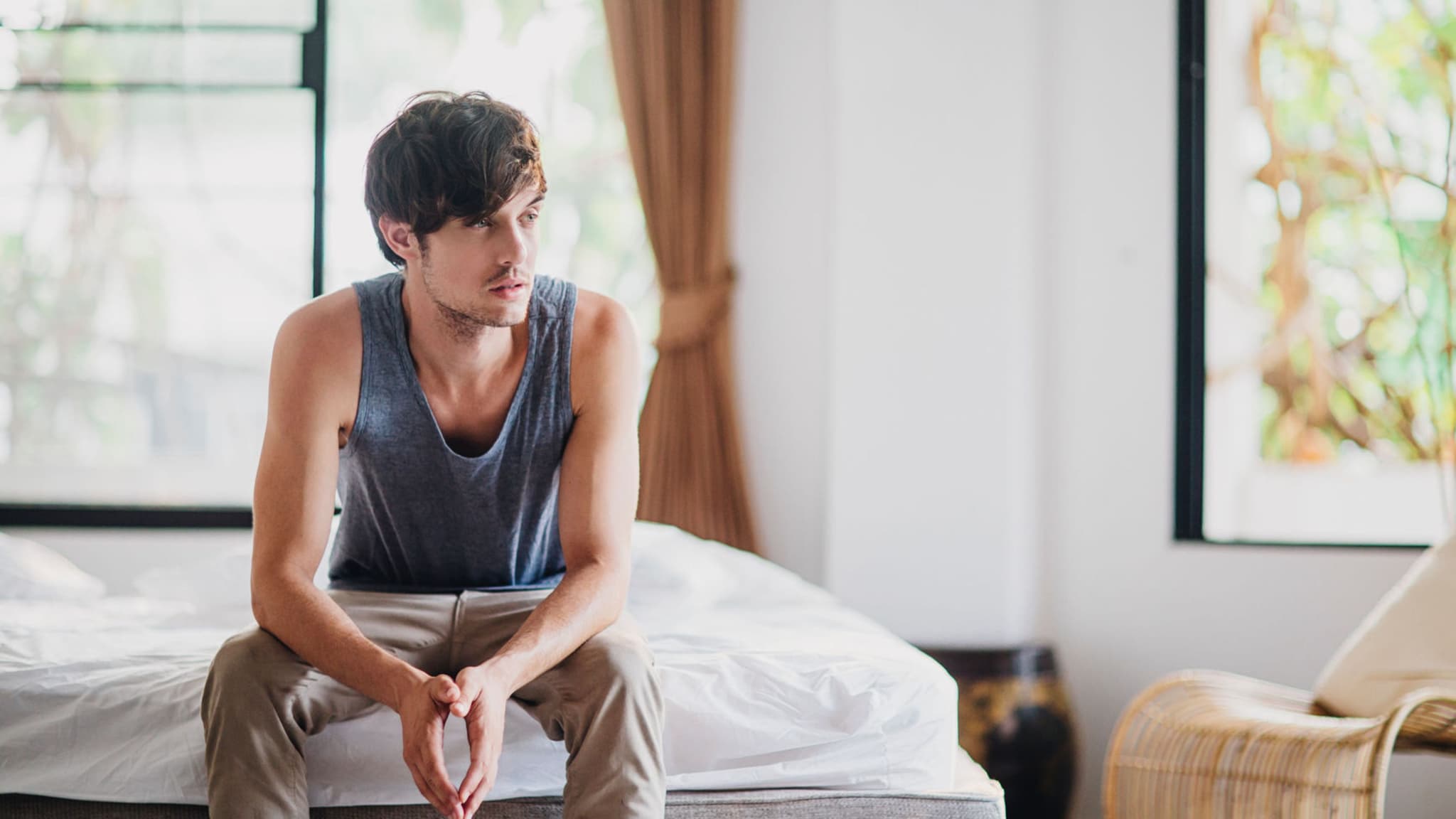 Erkrankungen: Junger Mann sitzt krank auf seinem Bett.