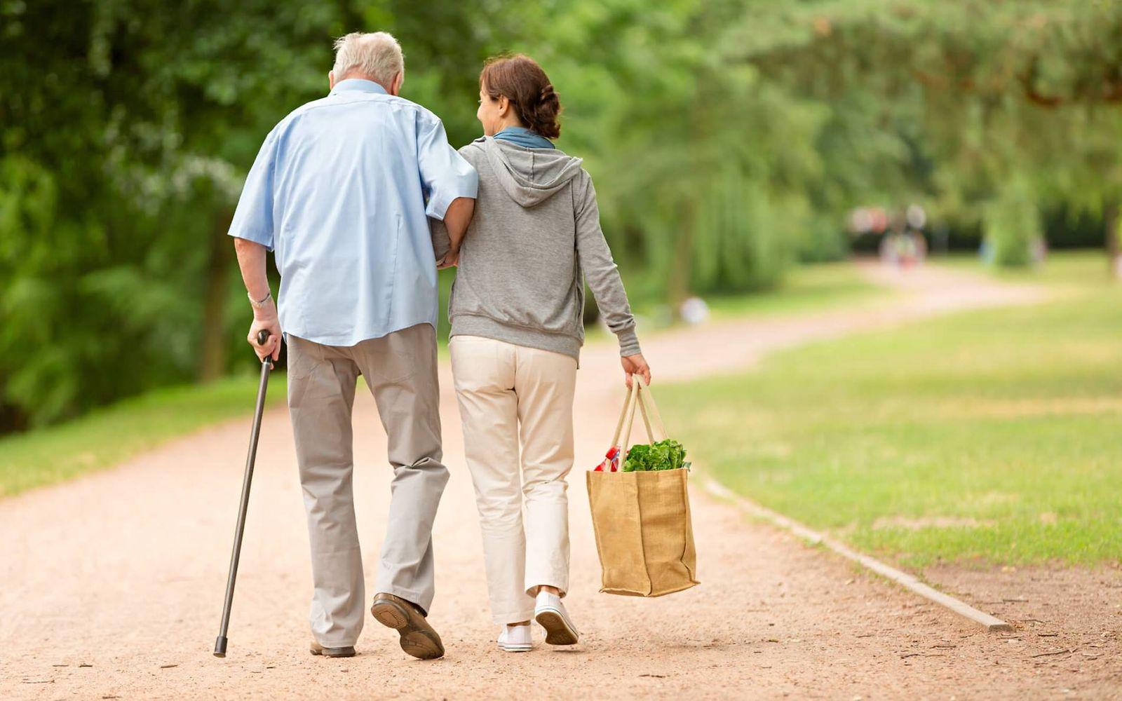 Pflege zu Hause: Junge Frau stützt älteren Mann beim Laufen im Park
