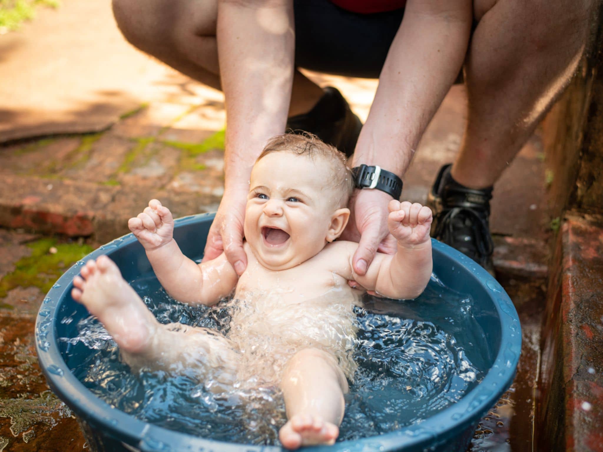 Babys und Hitze: Vater badet sein Baby draußen in einer kleinen Wanne