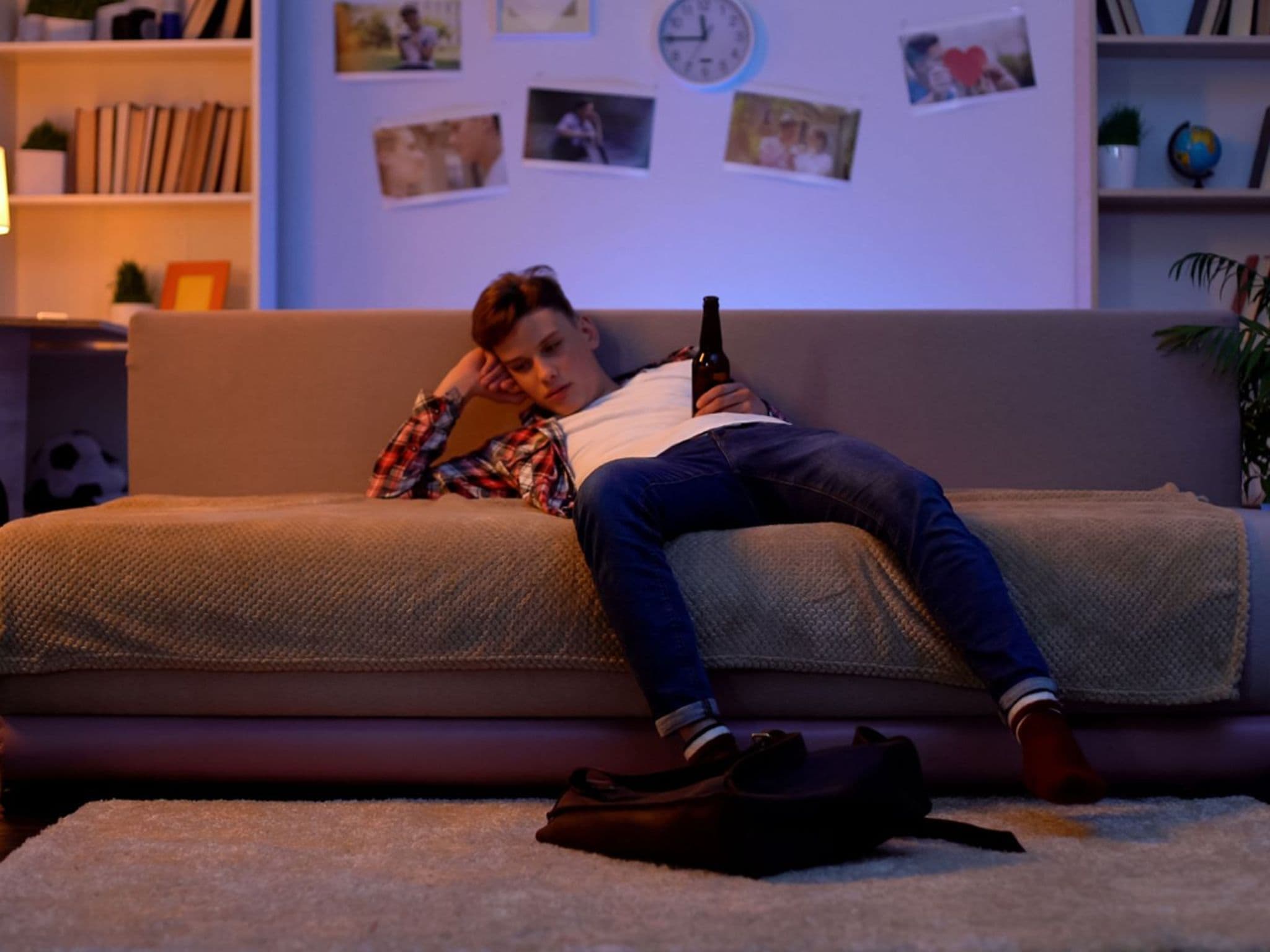 Sucht bei Kindern: Ein Teenager-Junge sitzt mit Bierflasche in der Hand auf dem Sofa