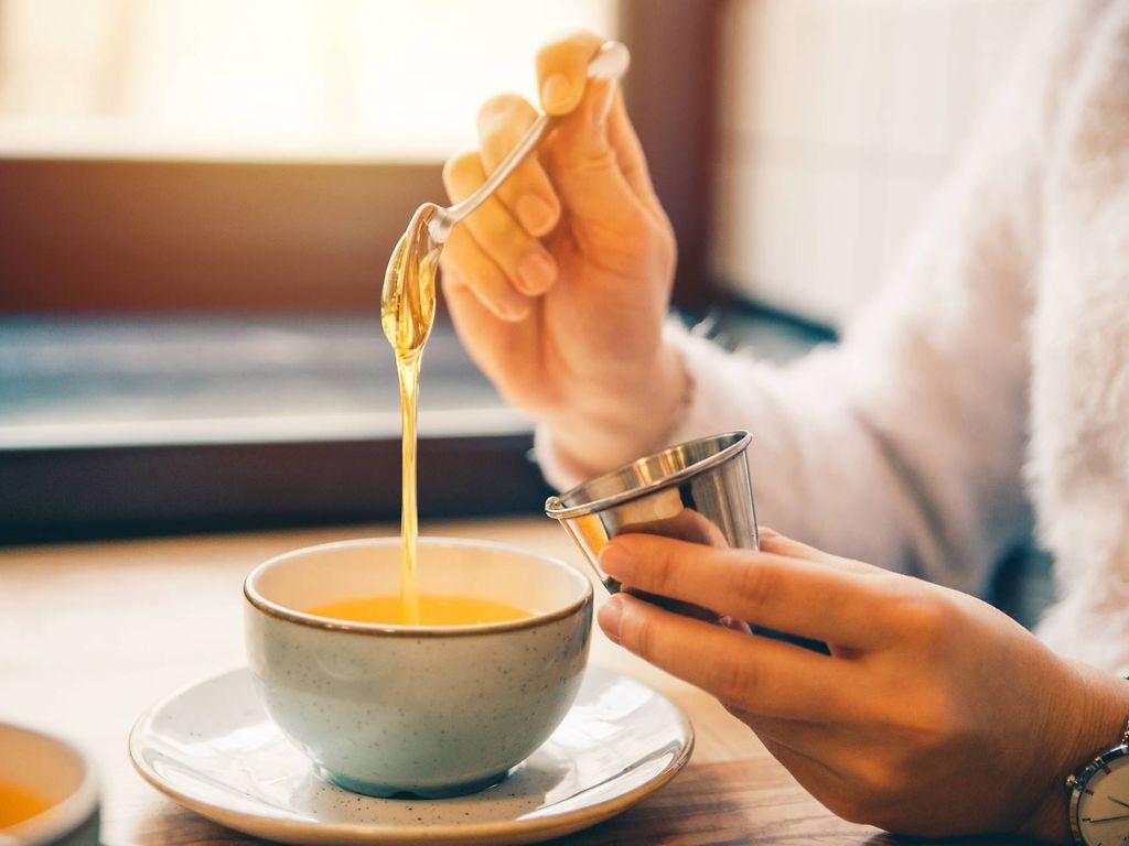 Zuckerersatz: Frau süßt ihren Tee mit einem Löffel Honig