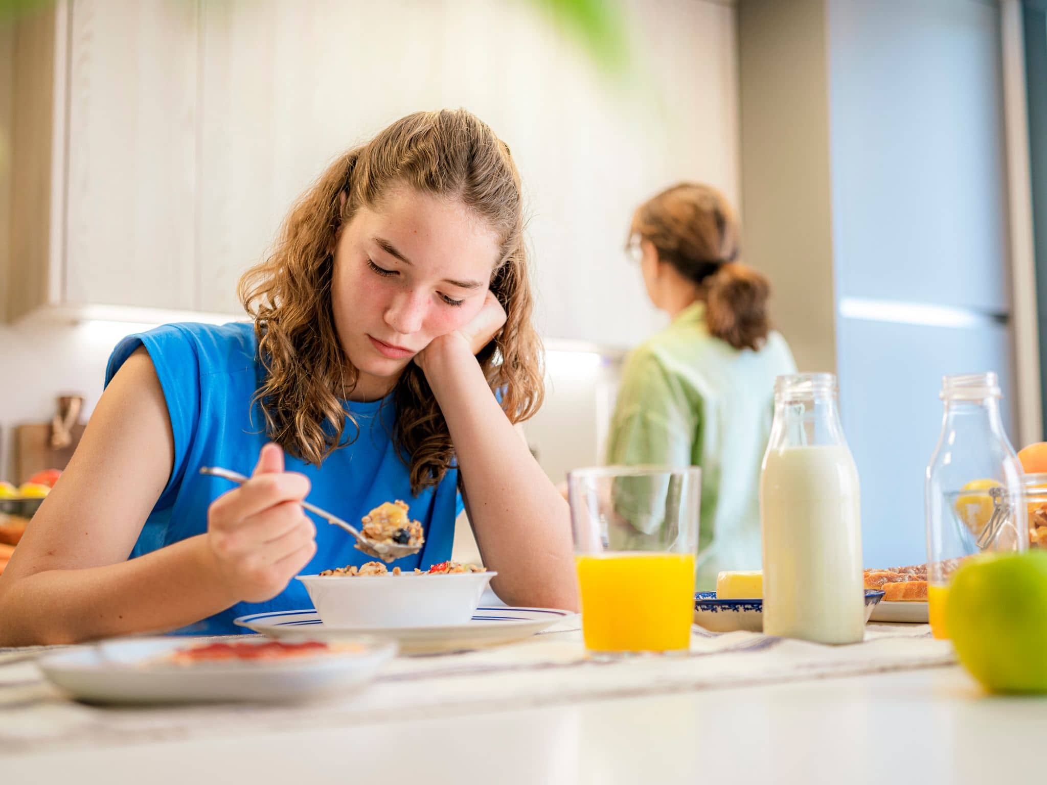 Esstörungen bei Kindern: Ein Mädchen im Teenageralter sitzt lustlos vor ihrer Müslischale