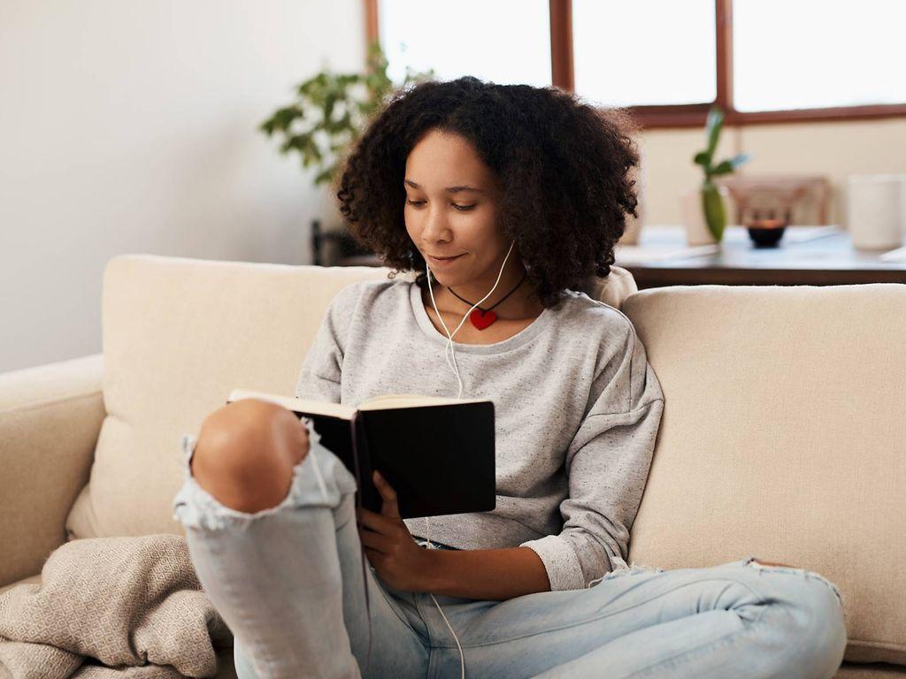 Tagebuch schreiben: Junge Frau sitzt entspannt auf der Couch und schreibt in ein Buch