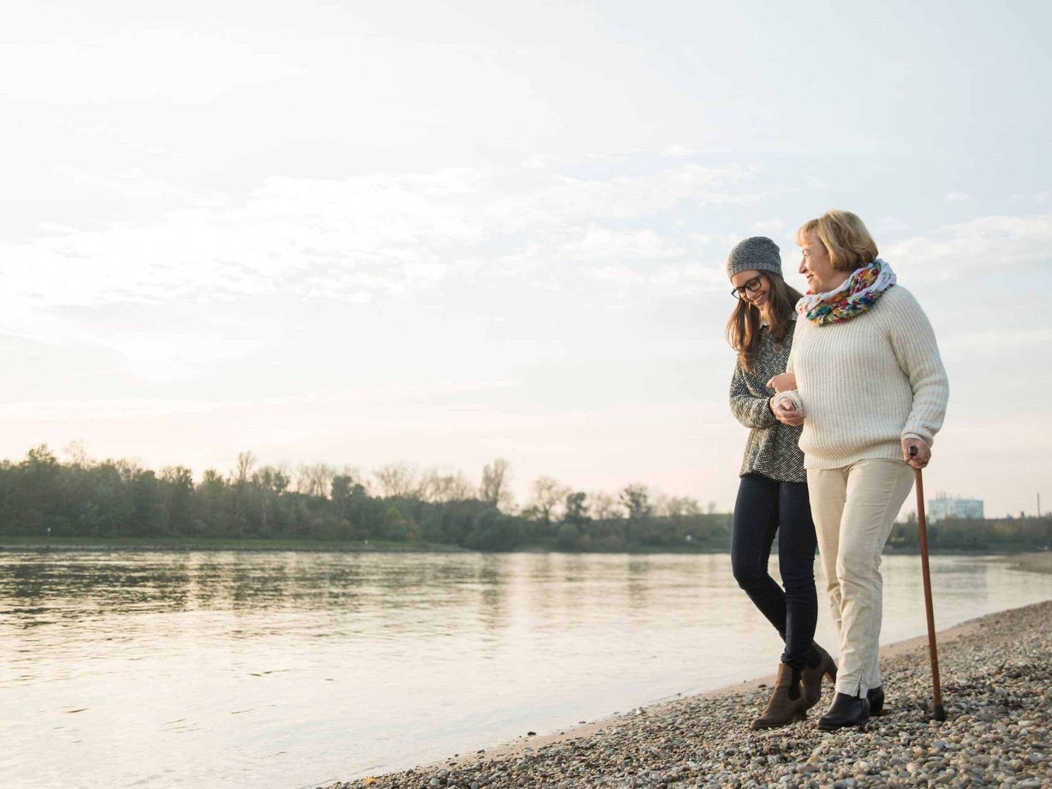 Pflege: Junge Frau spaziert mit ihrer Großmutter am Fluß entlang.