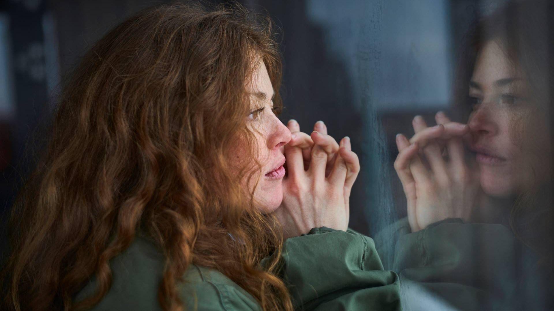 Symbolbild psychische Erkrankungen: Junge Frau schaut sorgenvoll aus dem Fenster