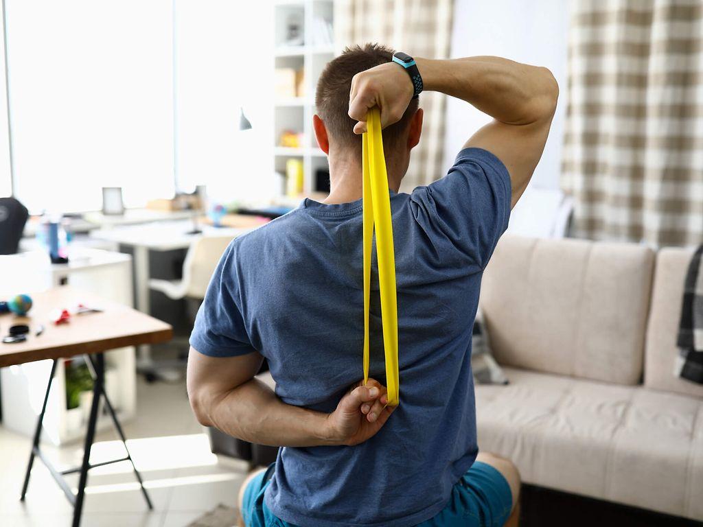 Bild: Online-Seminar Rückengesundheit: Mann benutzt gelbes Theraband hinter seinem Rücken.