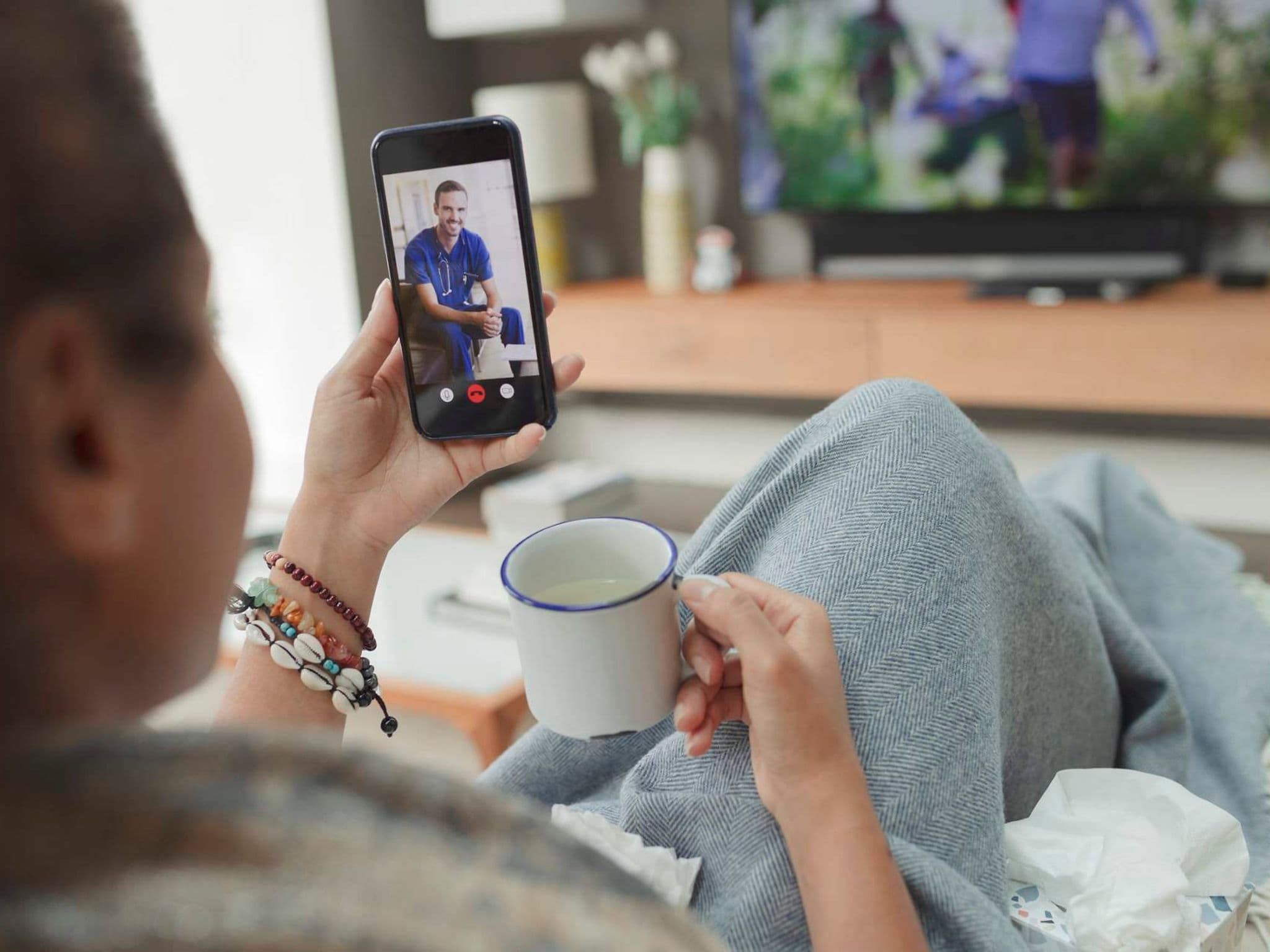 Bild: Frau sitzt auf dem Sofa zuhause und nutzt die Videosprechstunde.