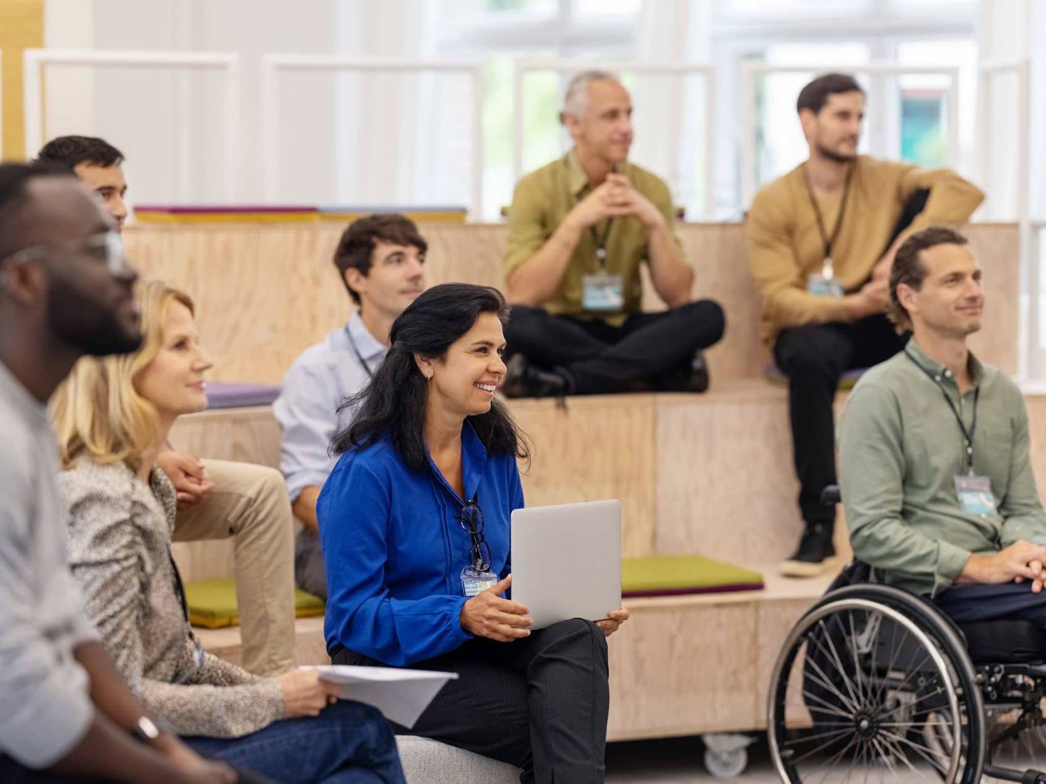 Bild: Personen sitzen auf einer kleinen Tribüne bei einer Veranstaltung und hören aufmerksam zu.