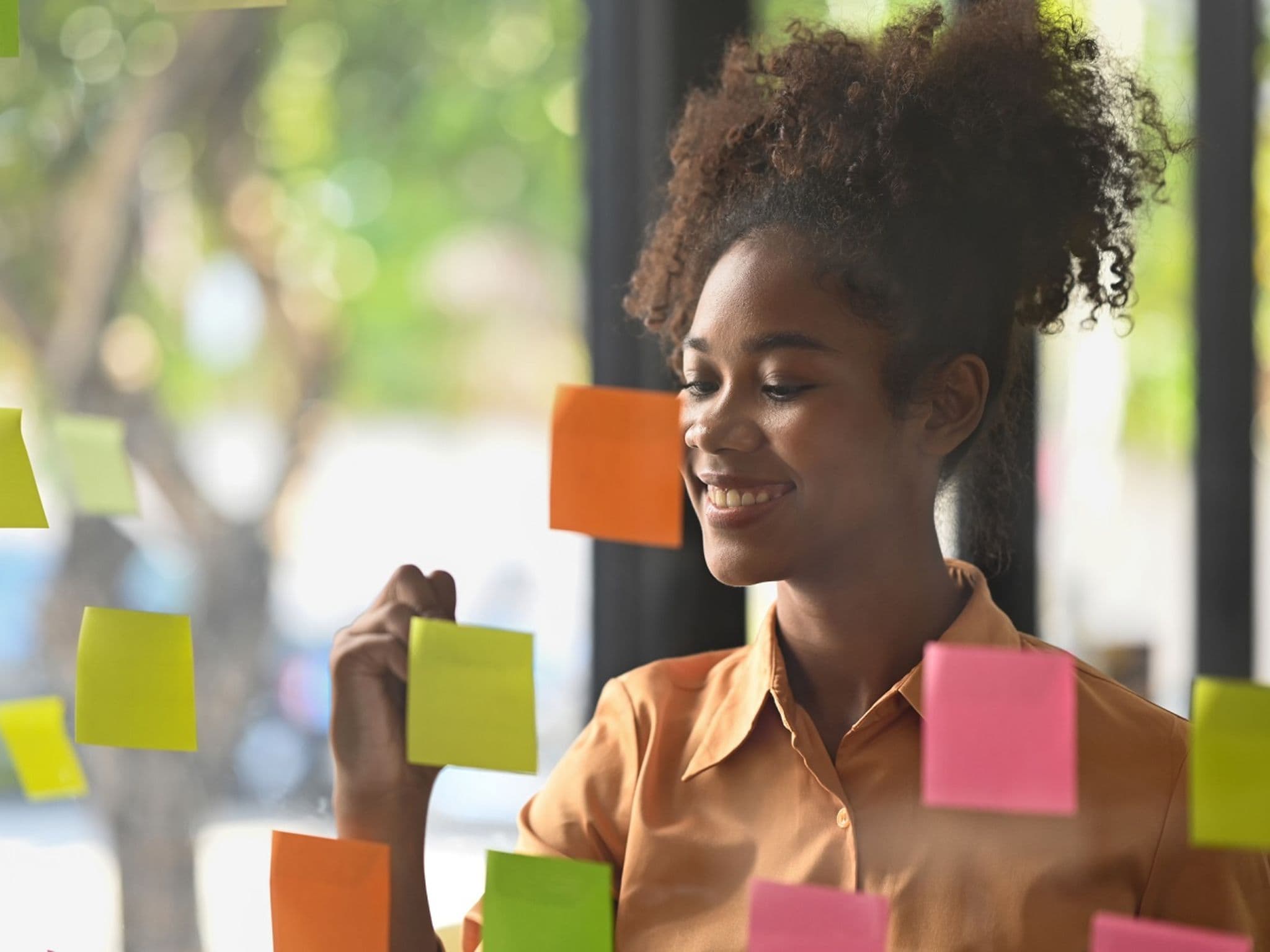 Junge Frau schreibt lächelnd auf Notizzettel an der Wand.