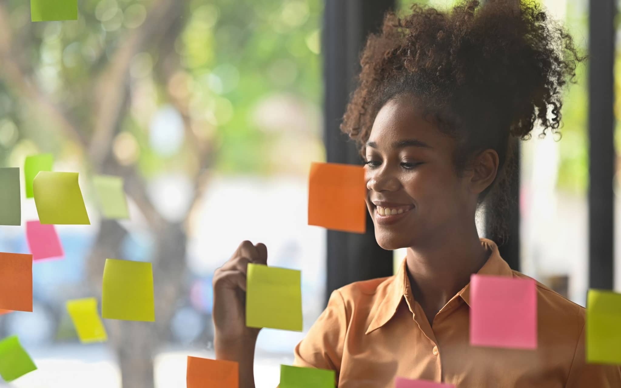 Junge Frau schreibt lächelnd auf Notizzettel an der Wand.