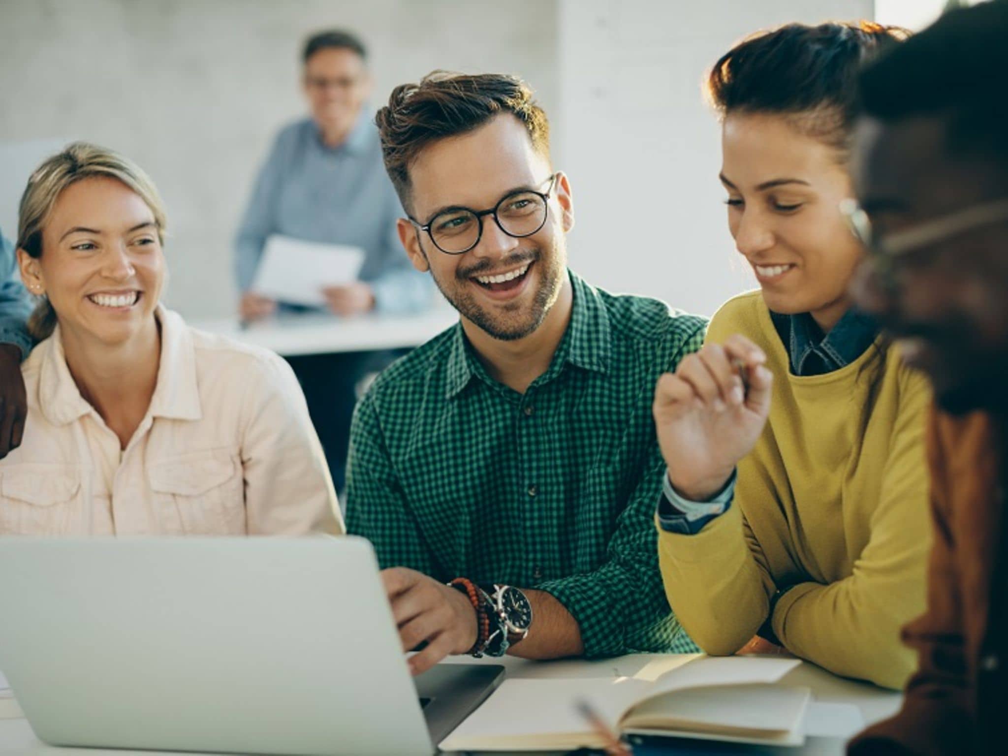 Gruppe sitzt am Tisch vor Laptop und lacht.