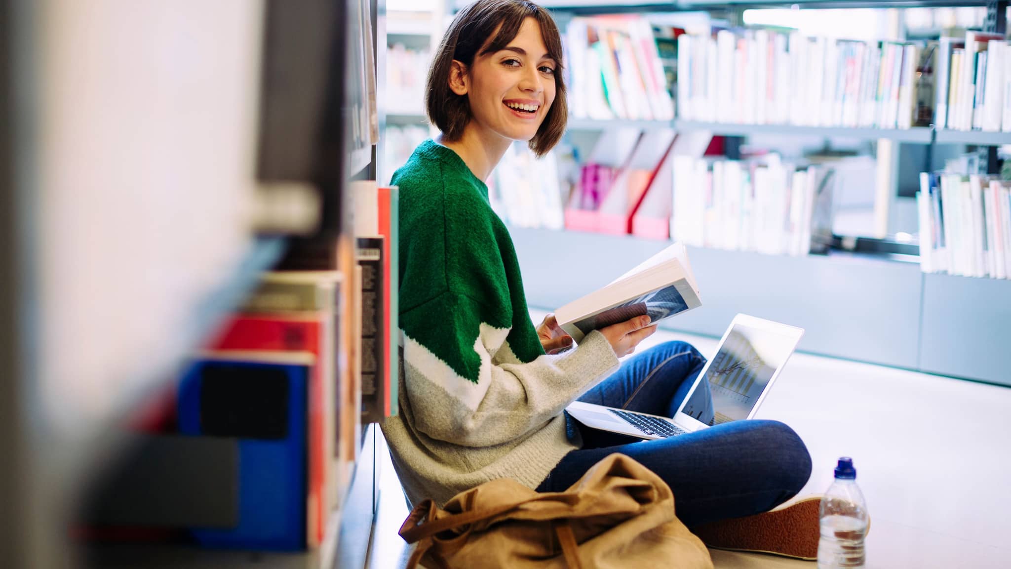 Leistungen für Studierende: Junge Frau sitzt auf dem Boden in einer Bibliothek.