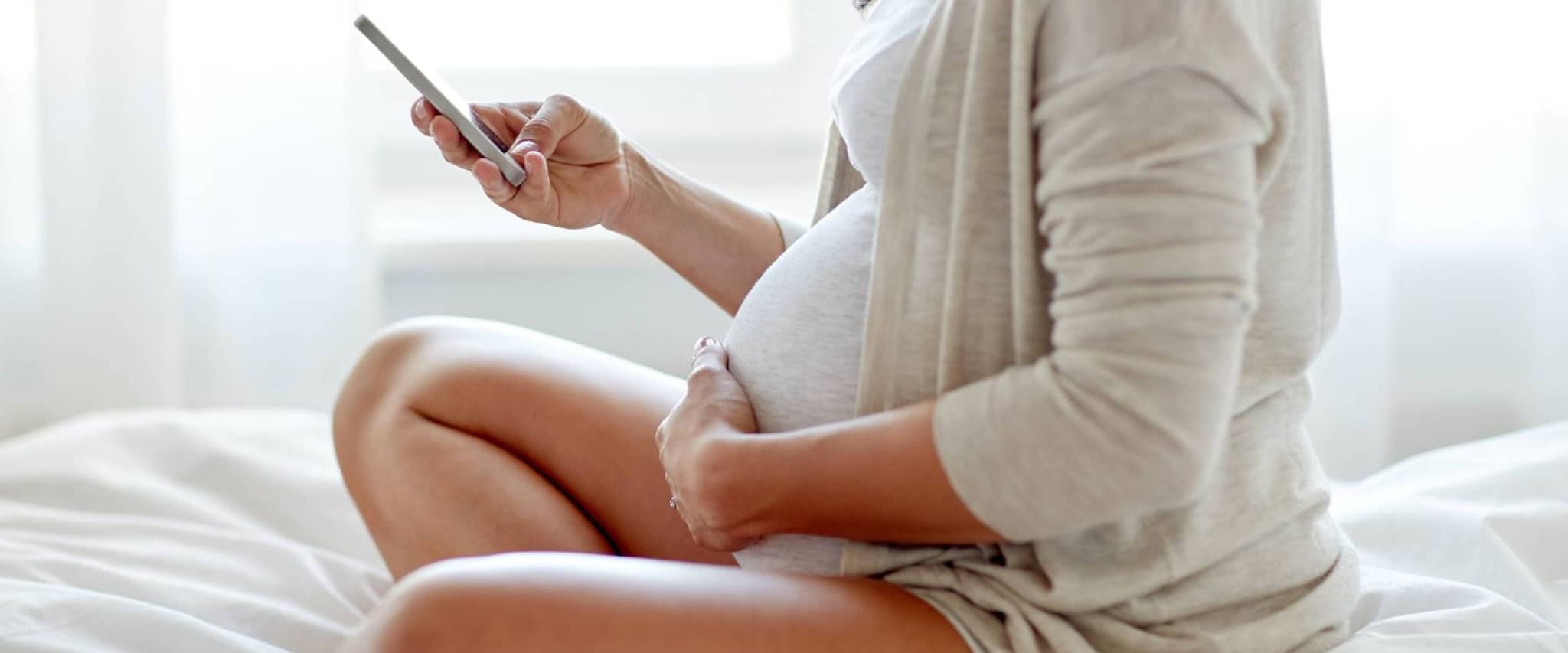 DAK MamaPLUS: Schwangere sitzt auf dem Bett und liest über das Vorsorgeprogramm