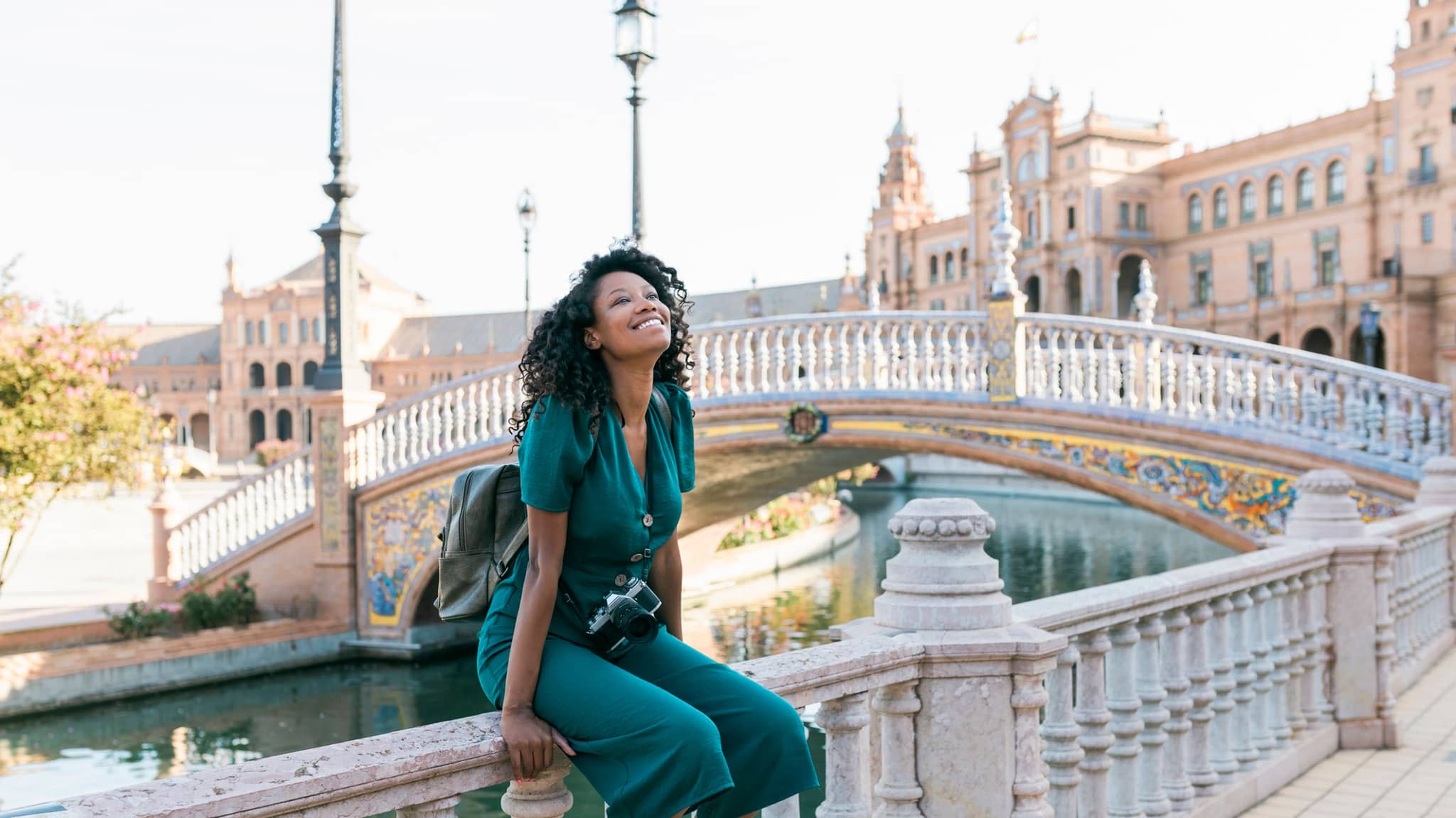 Langzeitaufenthalt Ausland: Junge Frau sitzt auf Geländer einer alten Brücke in Sevilla.