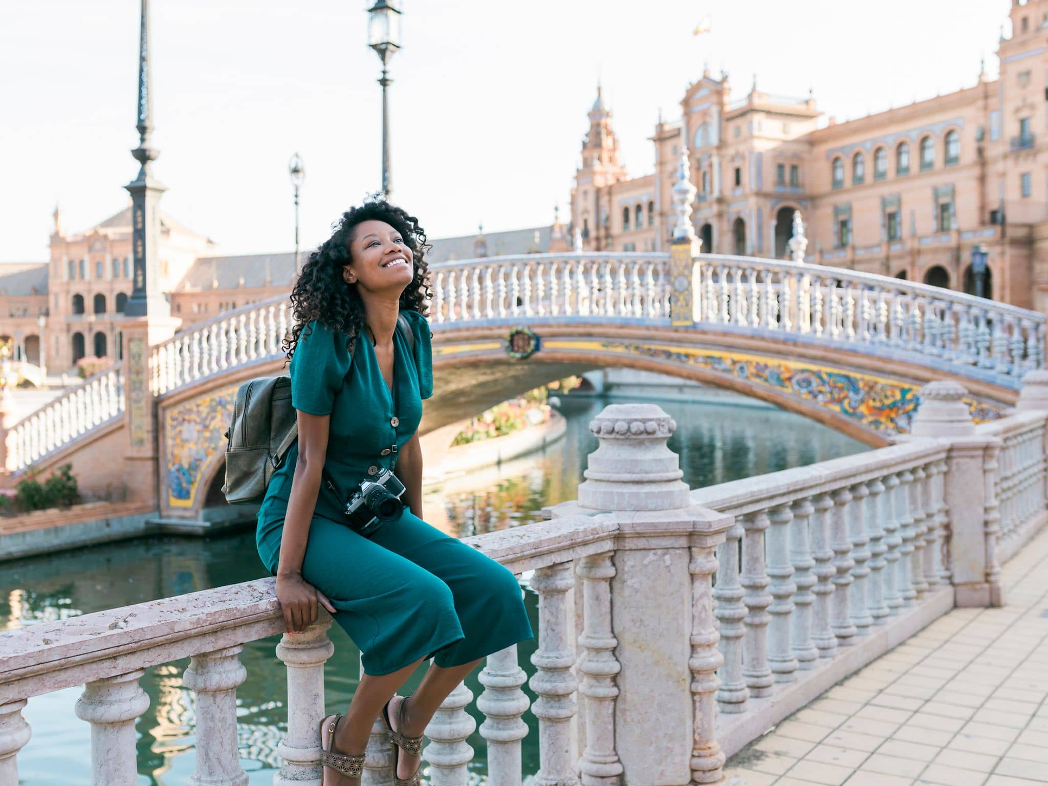 Langzeitaufenthalt Ausland: Junge Frau sitzt auf Geländer einer alten Brücke in Sevilla.