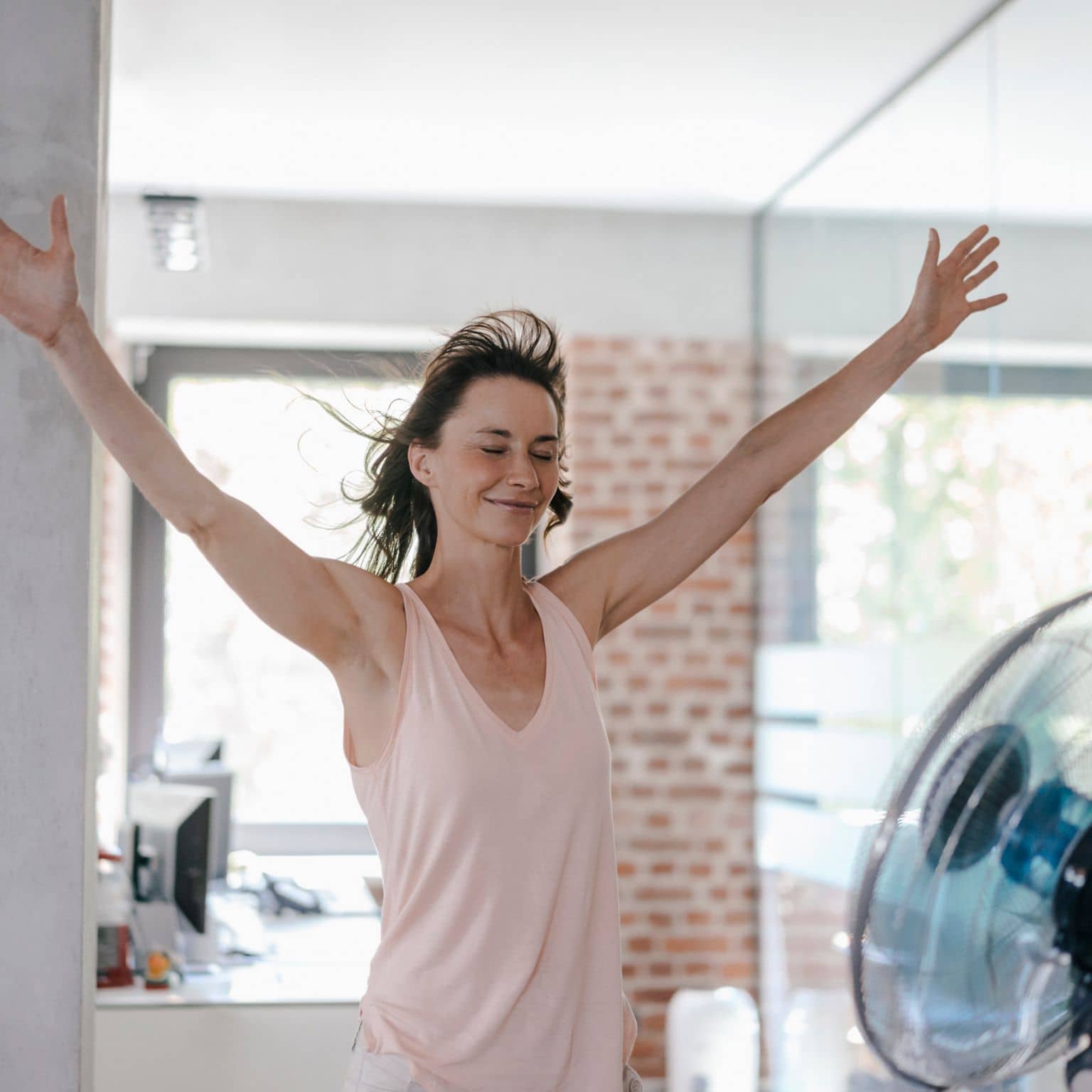 Frau bei Hitze im Büro vorm Ventilator
