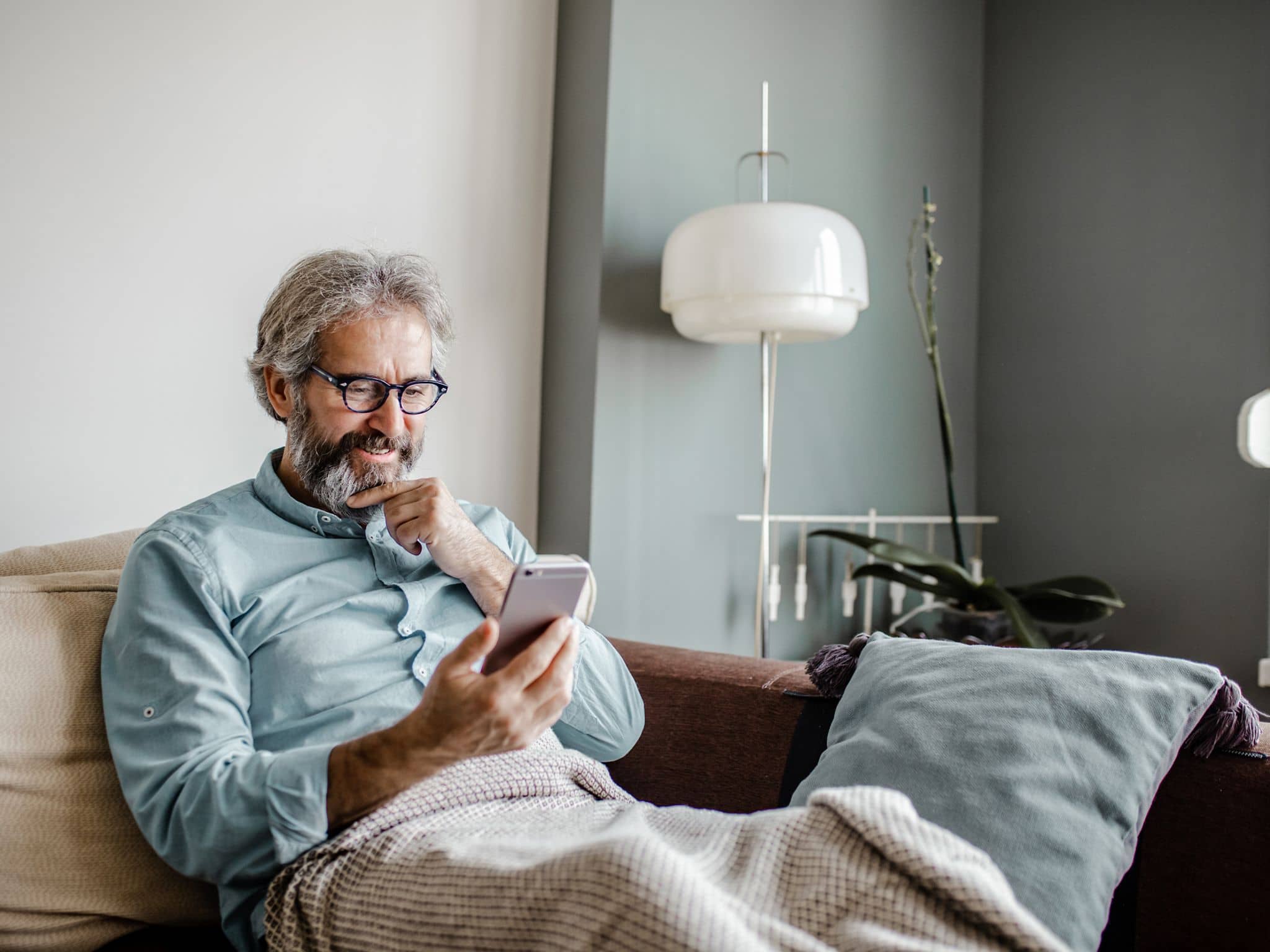 Zweitmeinung Gallenblase: Ein älterer Mann sitzt auf einem Sofa und liest auf seinem Smartphone