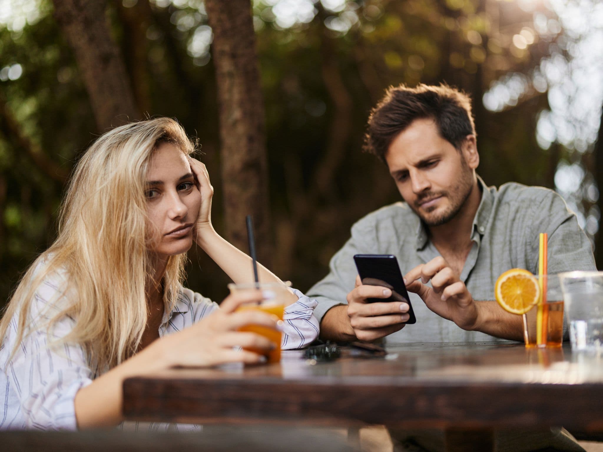 Eine Frau schaut genervt zur Seite, während ihr Partner Phubbing betreibt und am Smartphone hängt