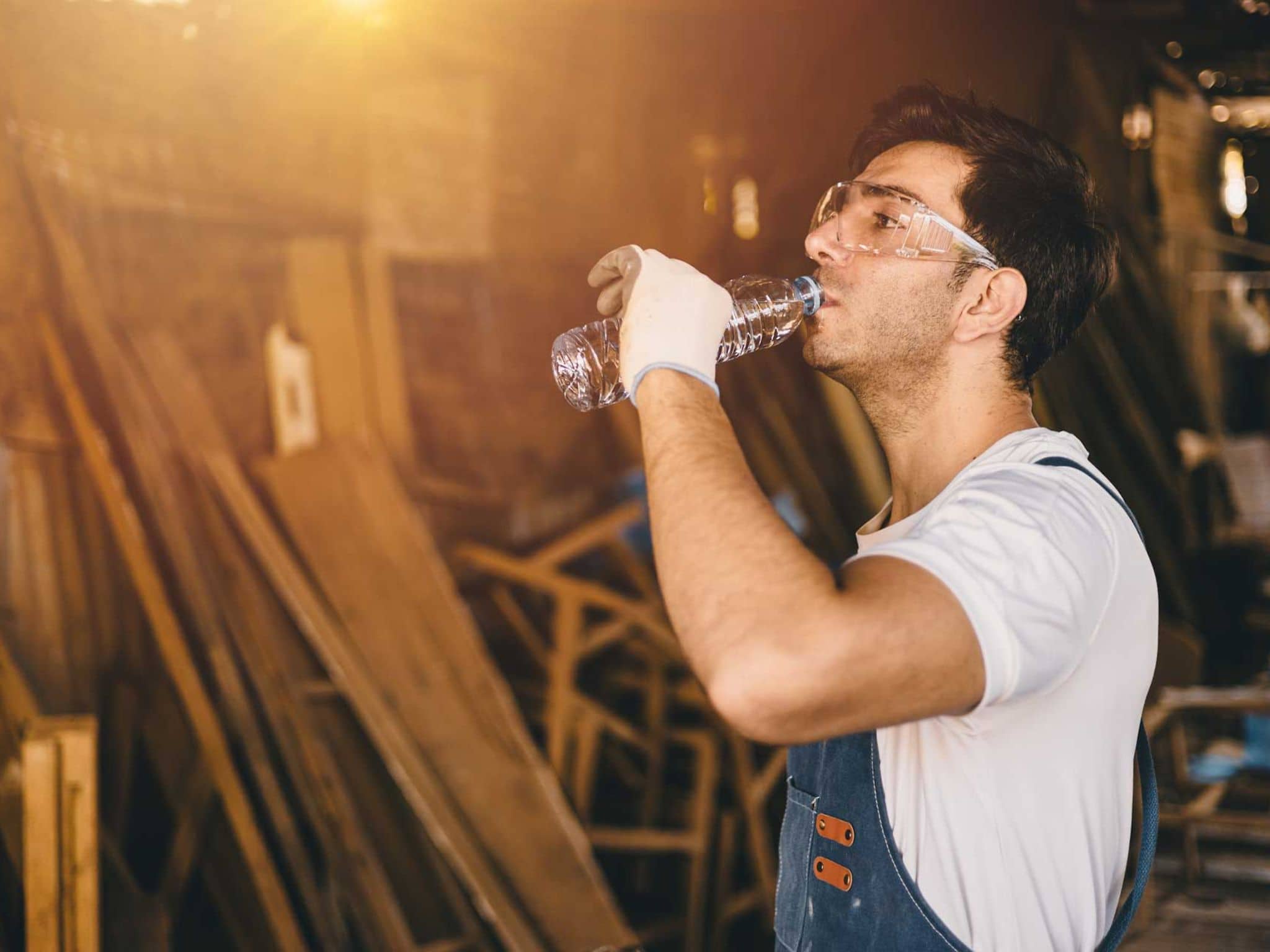Mann im Blaumann und mit Handschuhen trinkt aus einer Wasserflasche