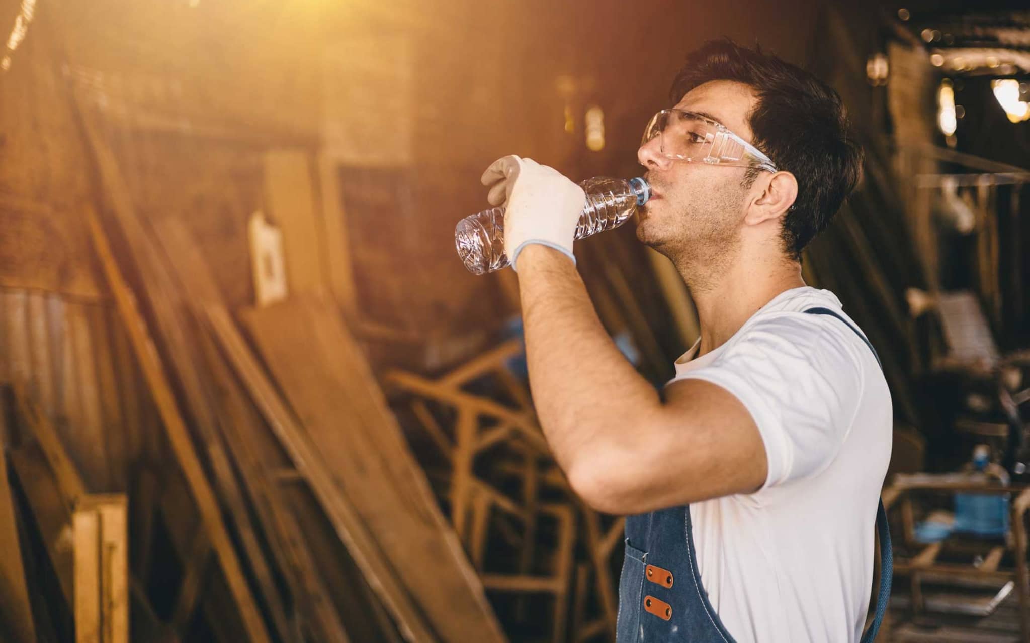 Mann im Blaumann und mit Handschuhen trinkt aus einer Wasserflasche