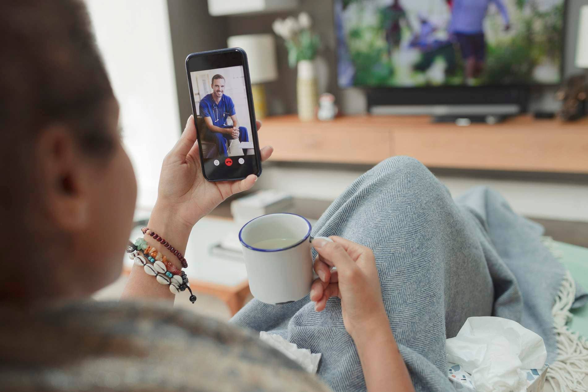 Bild: Frau sitzt auf dem Sofa zuhause und nutzt die Videosprechstunde.