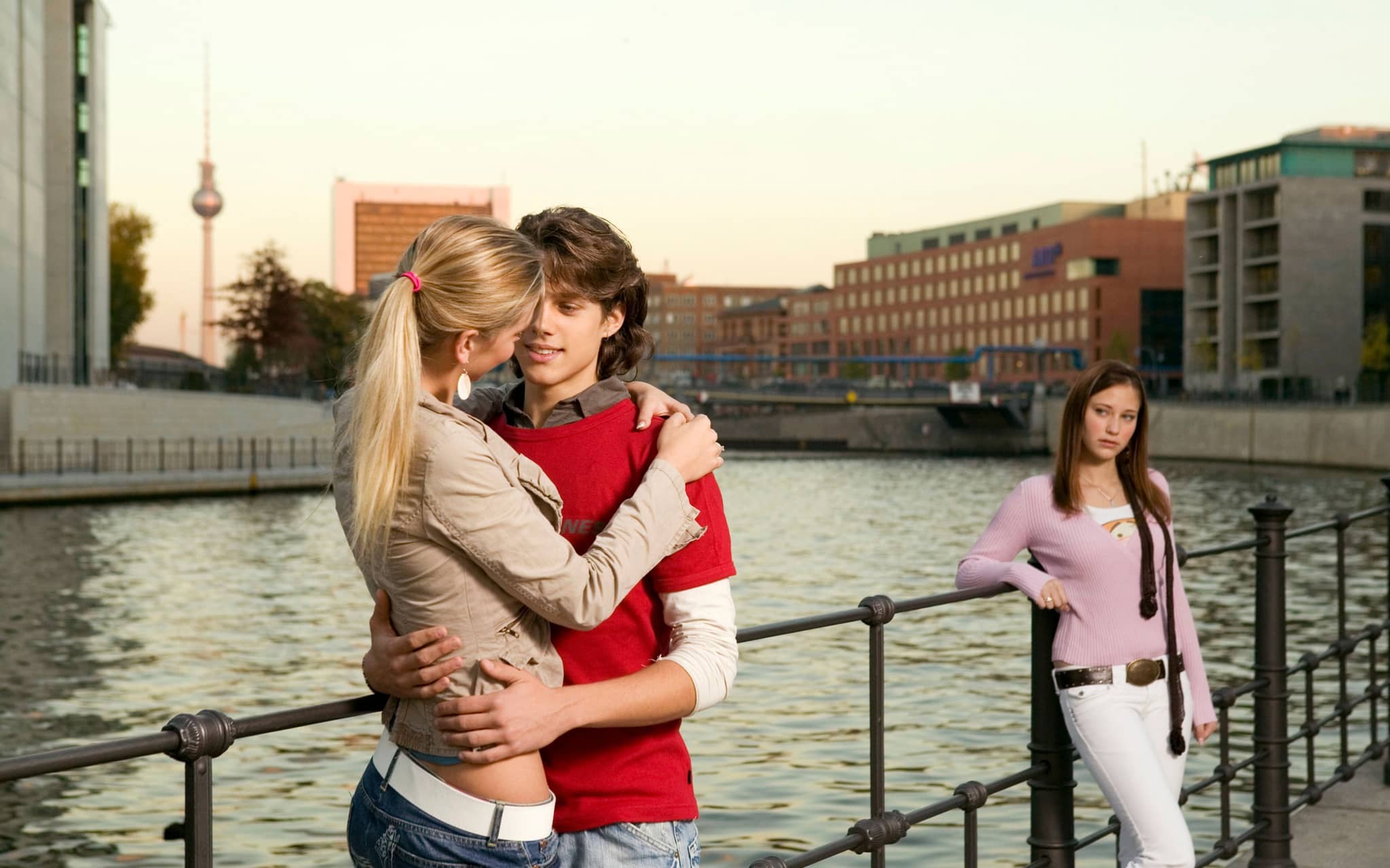 Symbolbild für Eifersucht: Ein junger Mann unterhält sich mit einer jungen Frau und eine andere junge Frau guckt eifersüchtig