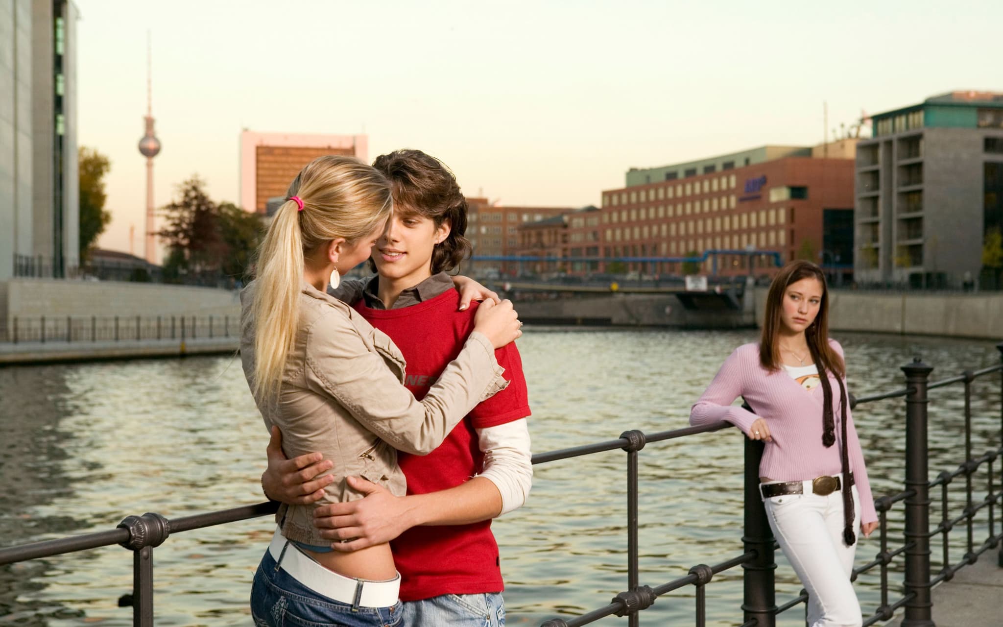 Symbolbild für Eifersucht: Ein junger Mann unterhält sich mit einer jungen Frau und eine andere junge Frau guckt eifersüchtig