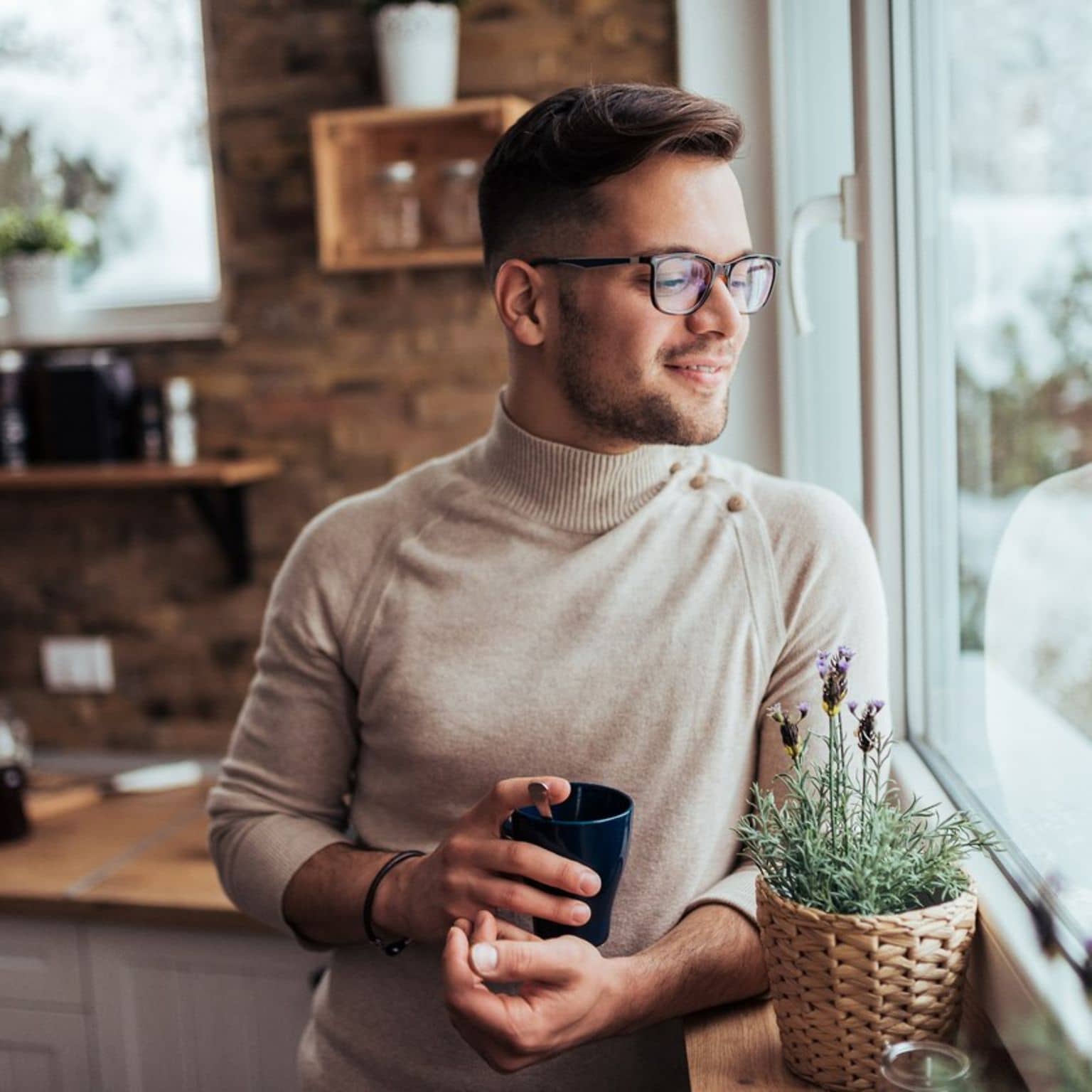 Junger Mann steht in der Küche und schaut aus dem Fenster.