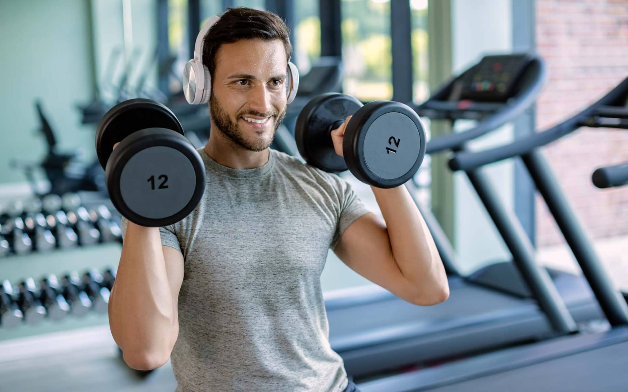 Junger Mann stemmt zwei Hanteln in einem Fitnessstudio.