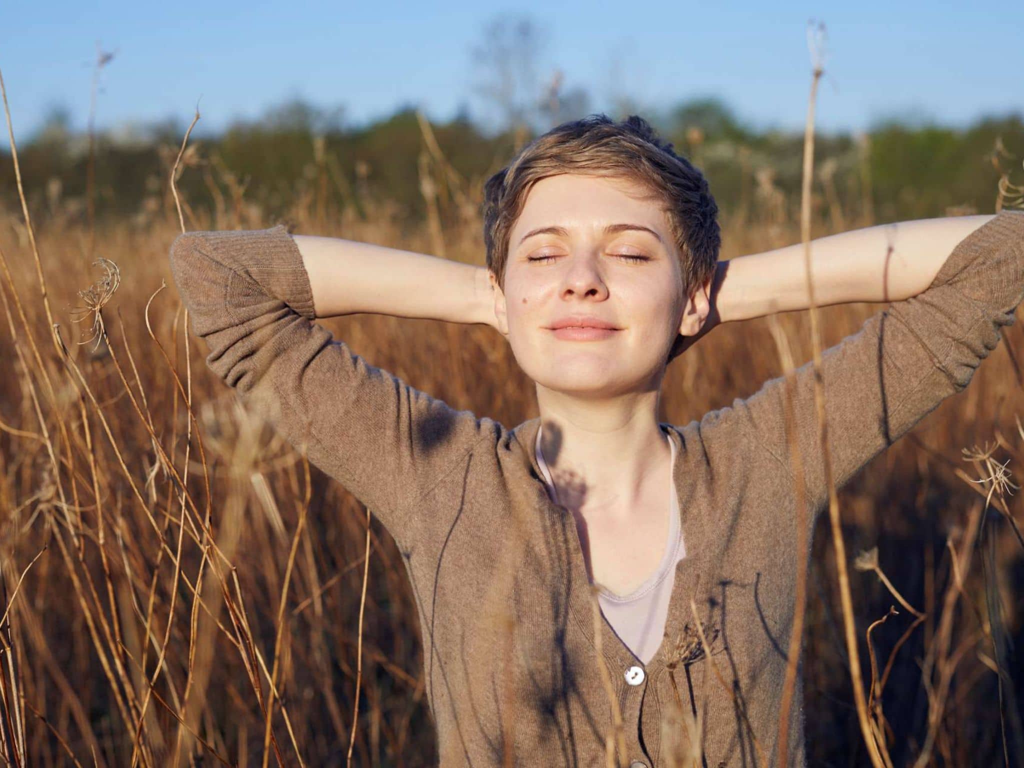 Junge Frau steht mit geschlossenen Augen in einem Kornfeld und sonnt sich.