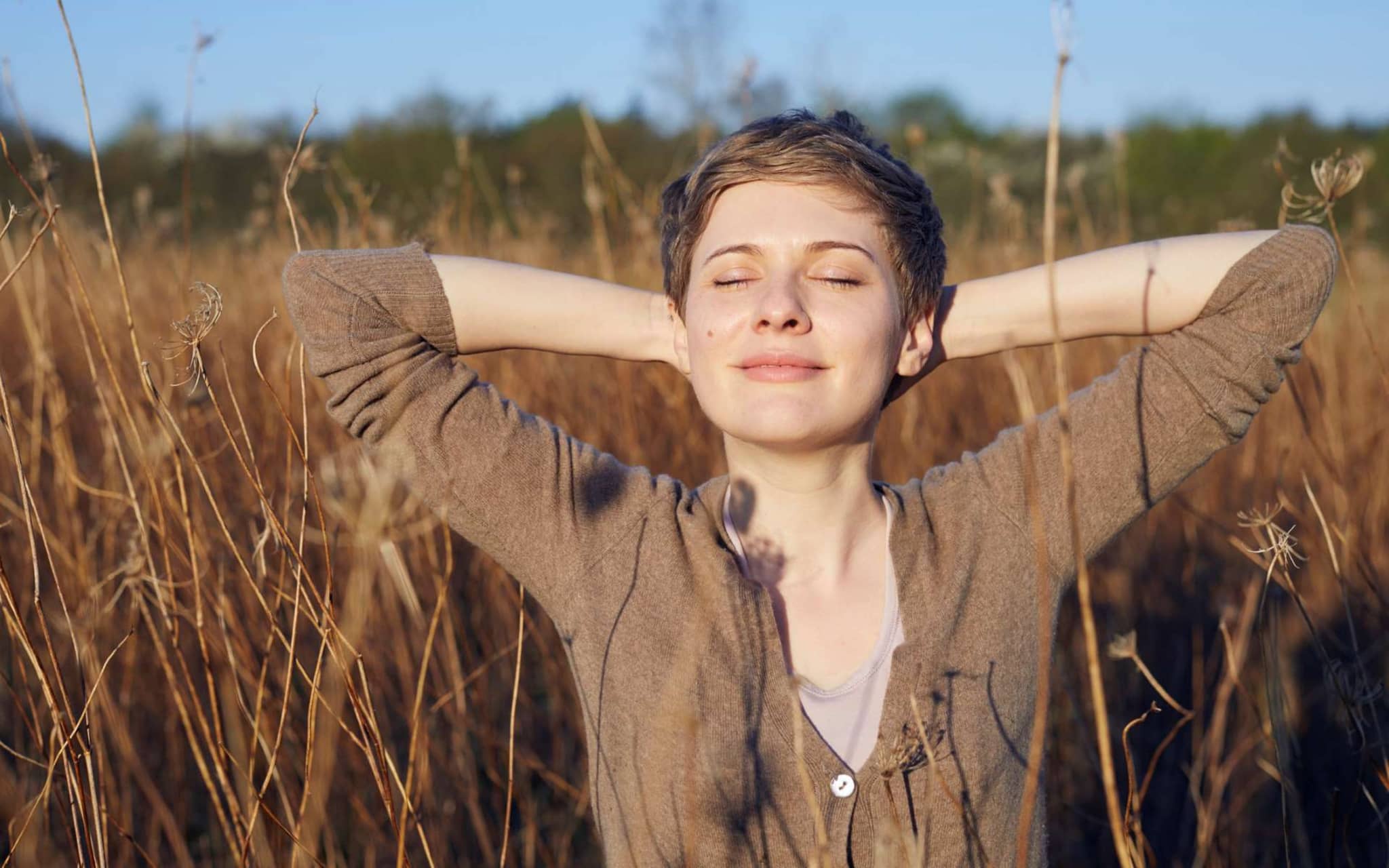 Junge Frau steht mit geschlossenen Augen in einem Kornfeld und sonnt sich.
