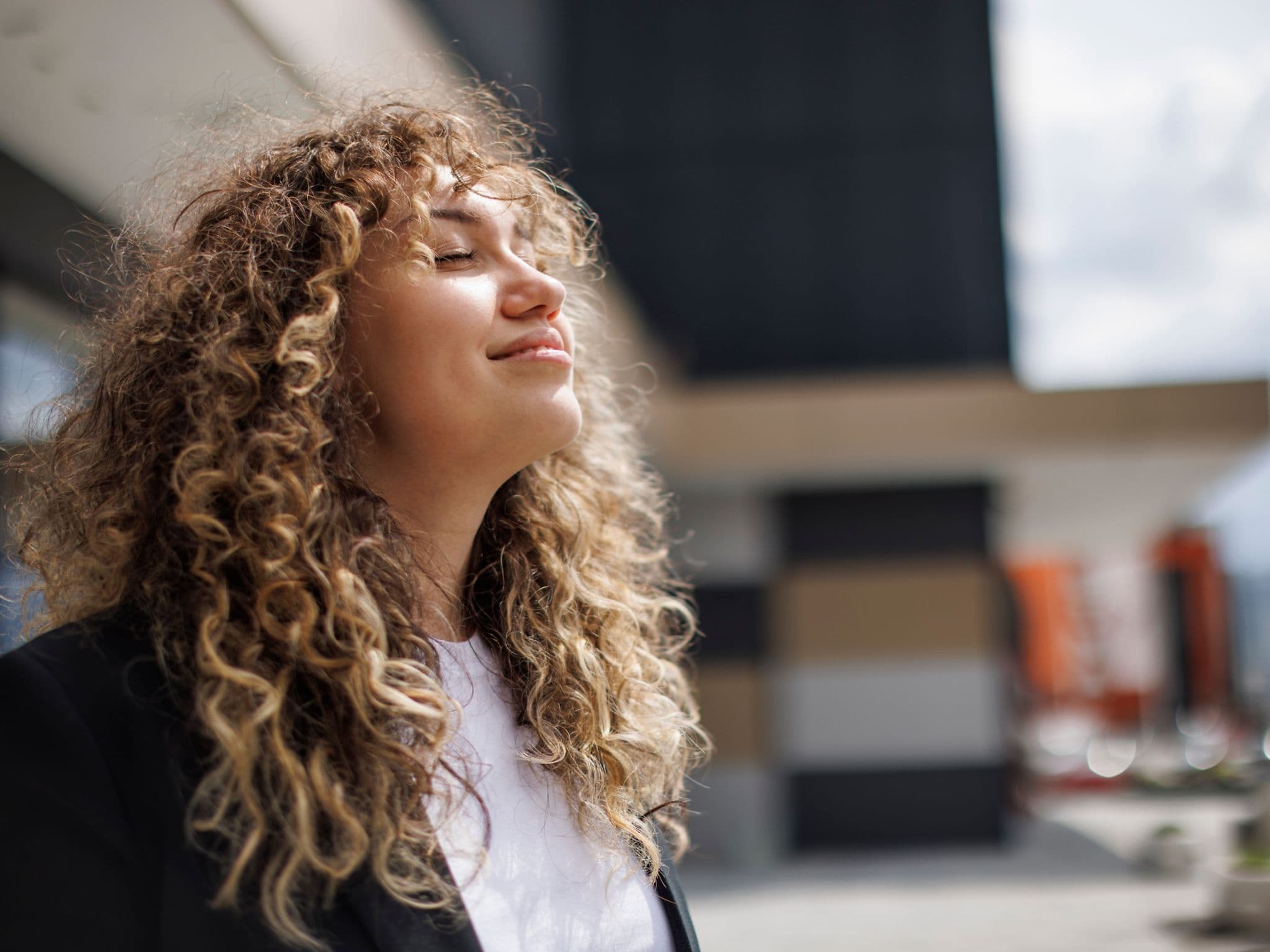 Benefits at DAK: Young woman with curls enjoying the sun with her eyes closed.