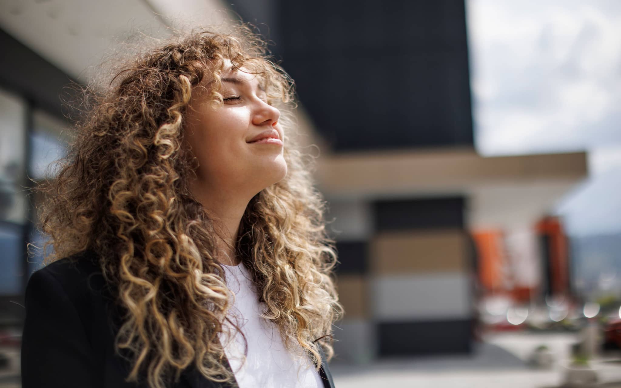 Benefits at DAK: Young woman with curls enjoying the sun with her eyes closed.
