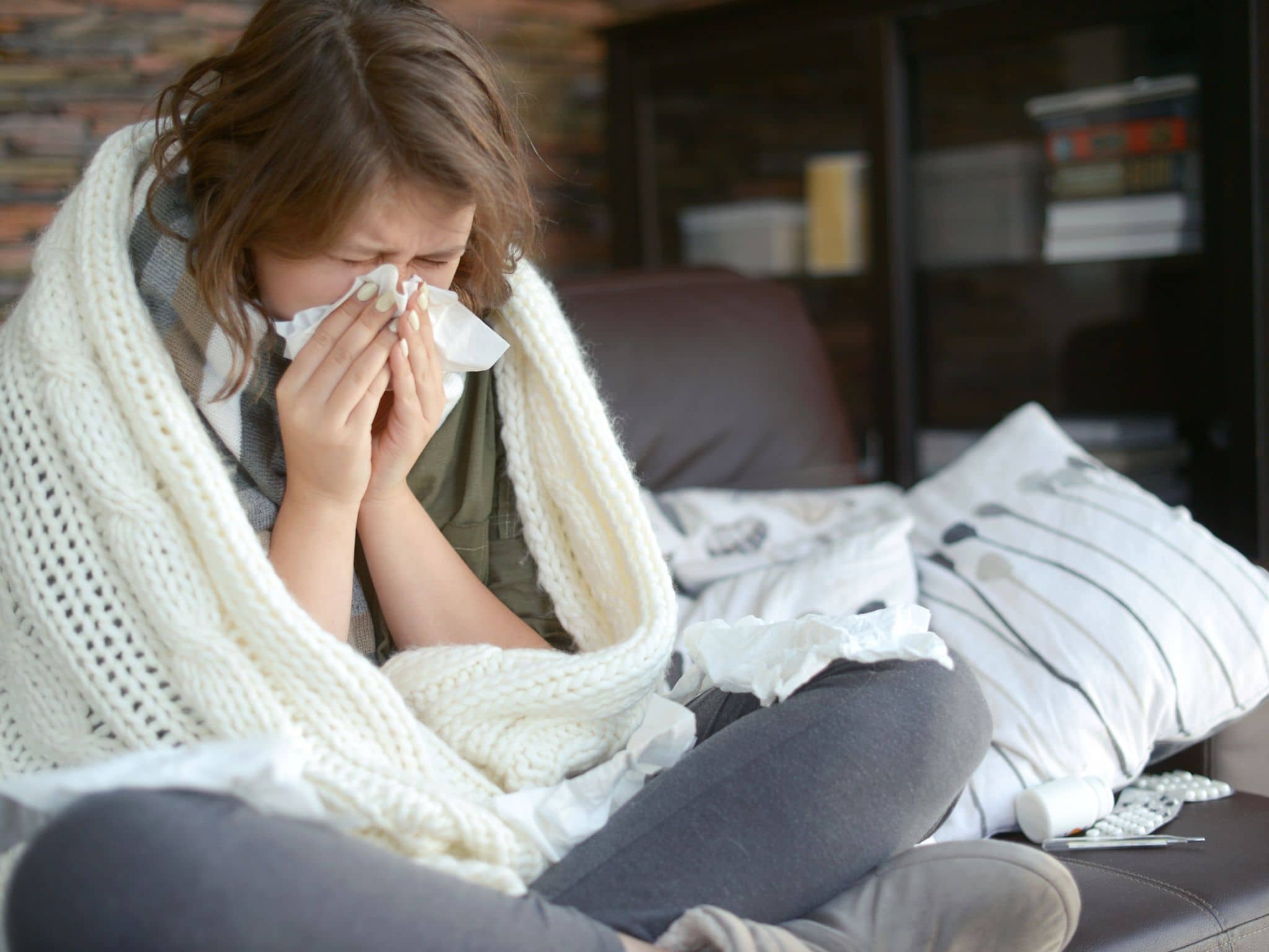 Ständig erkältet: Eine junge Frau sitzt auf einem Sofa und schnupft in ihr Taschentuch