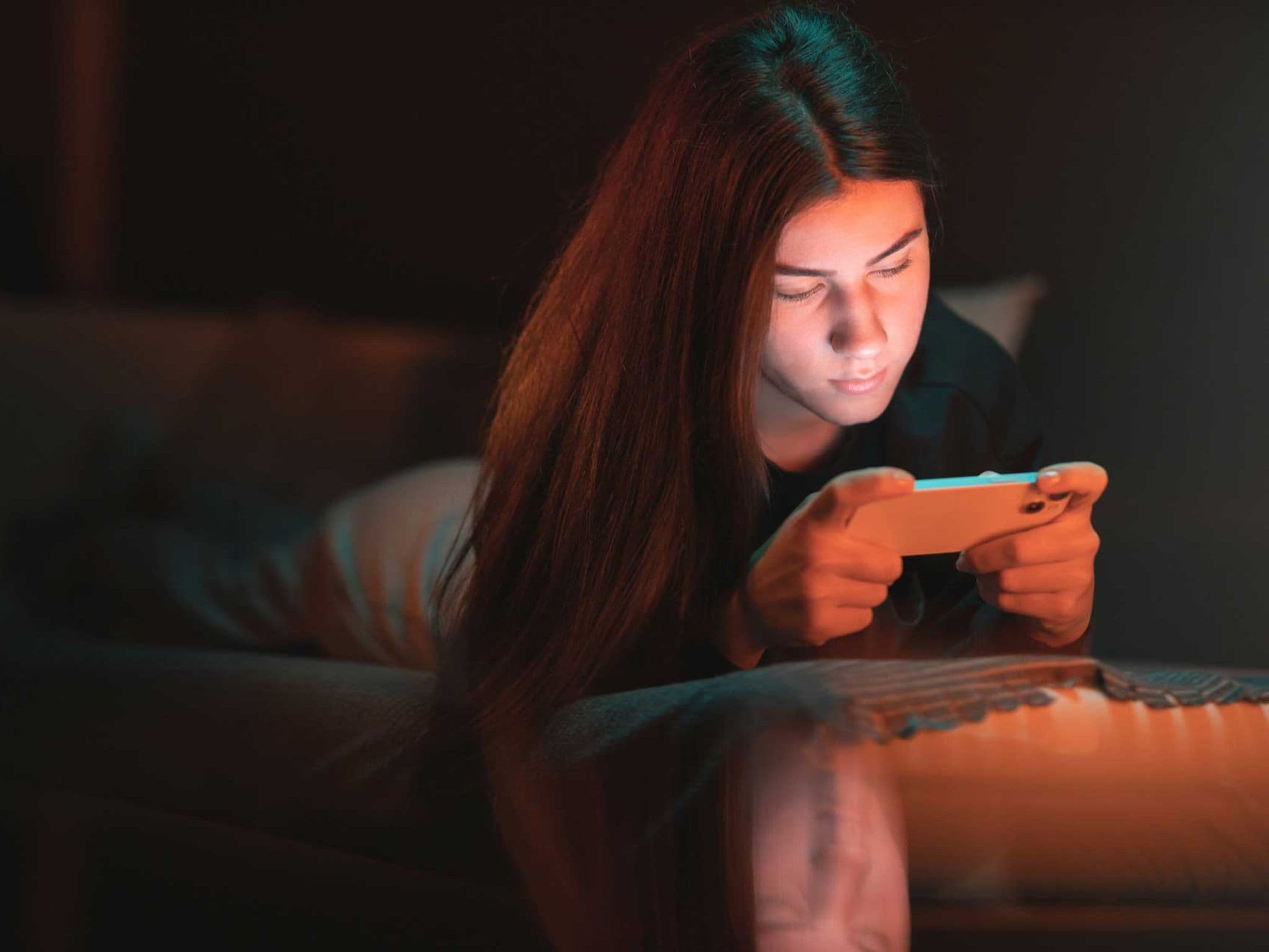 Symbolbild Social-Media-Sucht: Mädchen liegt im Dunkeln auf dem Bett und hat Smartphone in der Hand