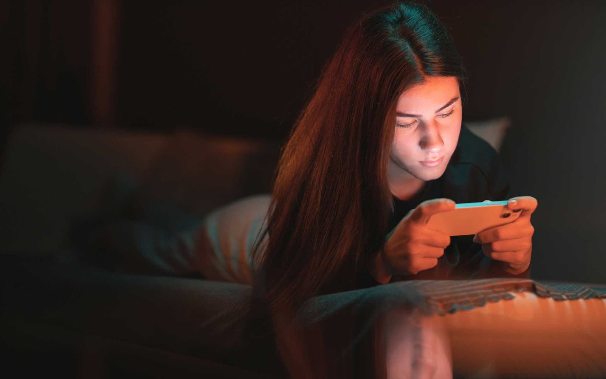 Symbolbild Social-Media-Sucht: Mädchen liegt im Dunkeln auf dem Bett und hat Smartphone in der Hand