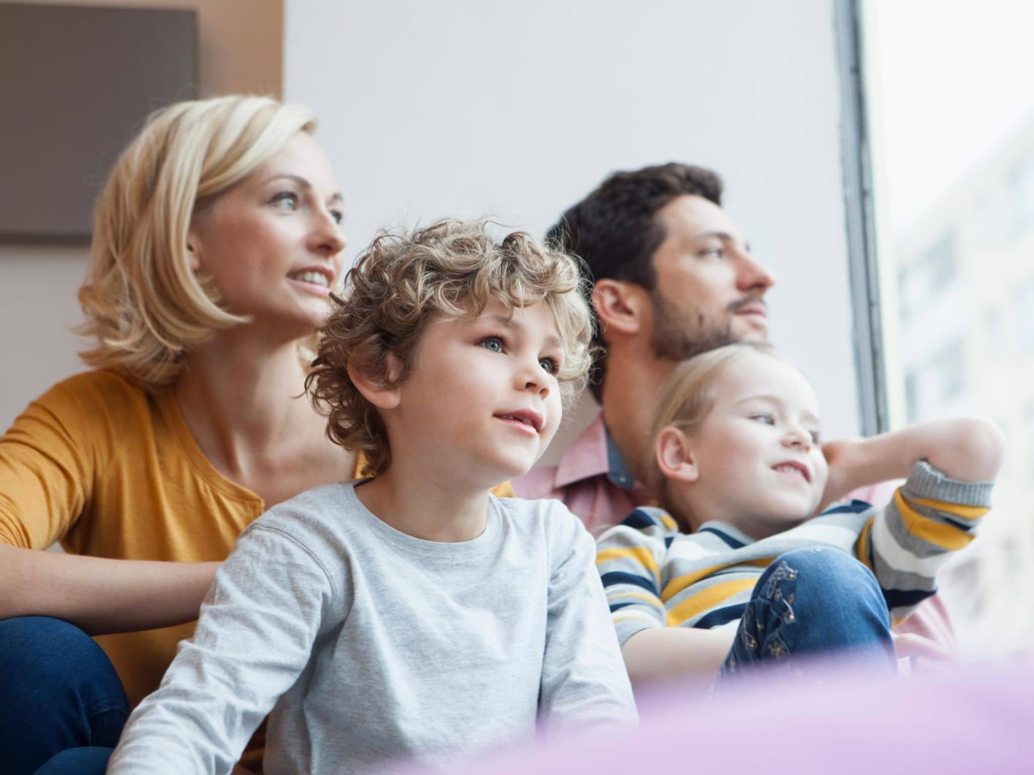 Familie mit zwei kleinen Kindern schaut gemeinsam aus dem Fenster.