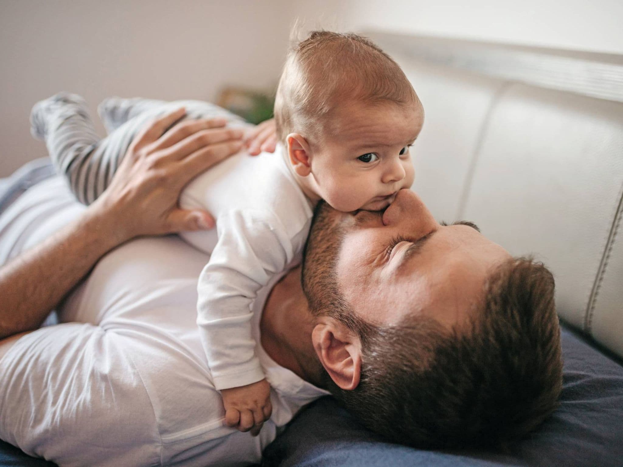 Bild: Junger Vater liegt auf dem Sofa und gibt seinem Baby einen Kuss.