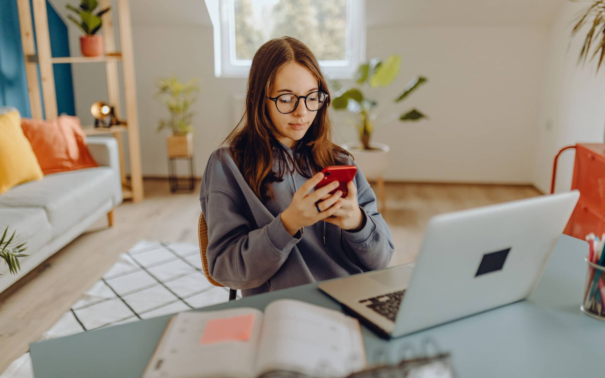 Image: Young woman sitting at her desk looking at her smartphone.