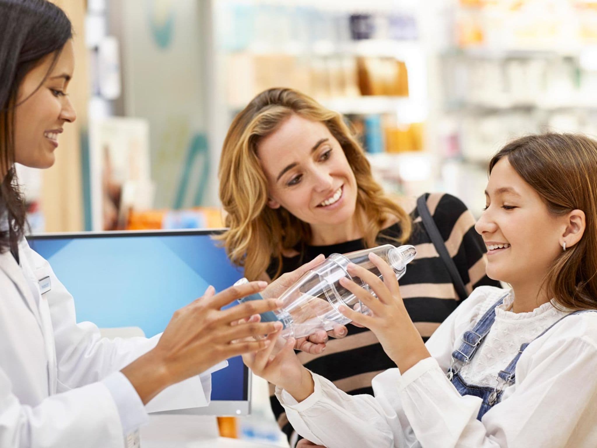 Pharmazeutische Dienstleistungen: Apothekerin erklärt einem Mädchen und seiner Mutter die Handhabung eines Inhalators.